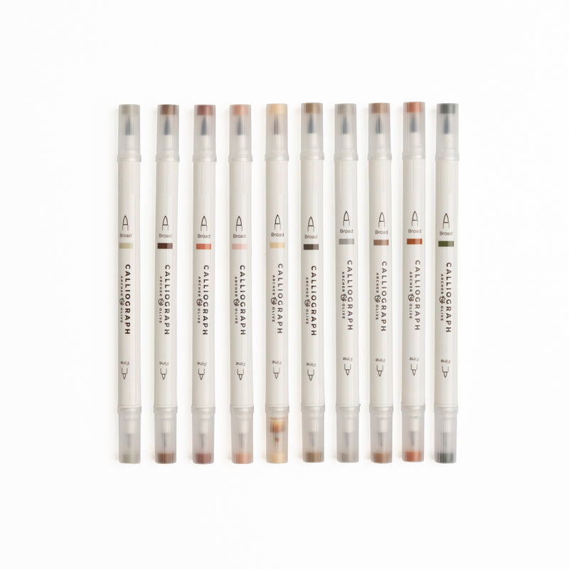 Set of ten Quiet Corners calligraphy pens with flexible brush tips laid out with lettering samples